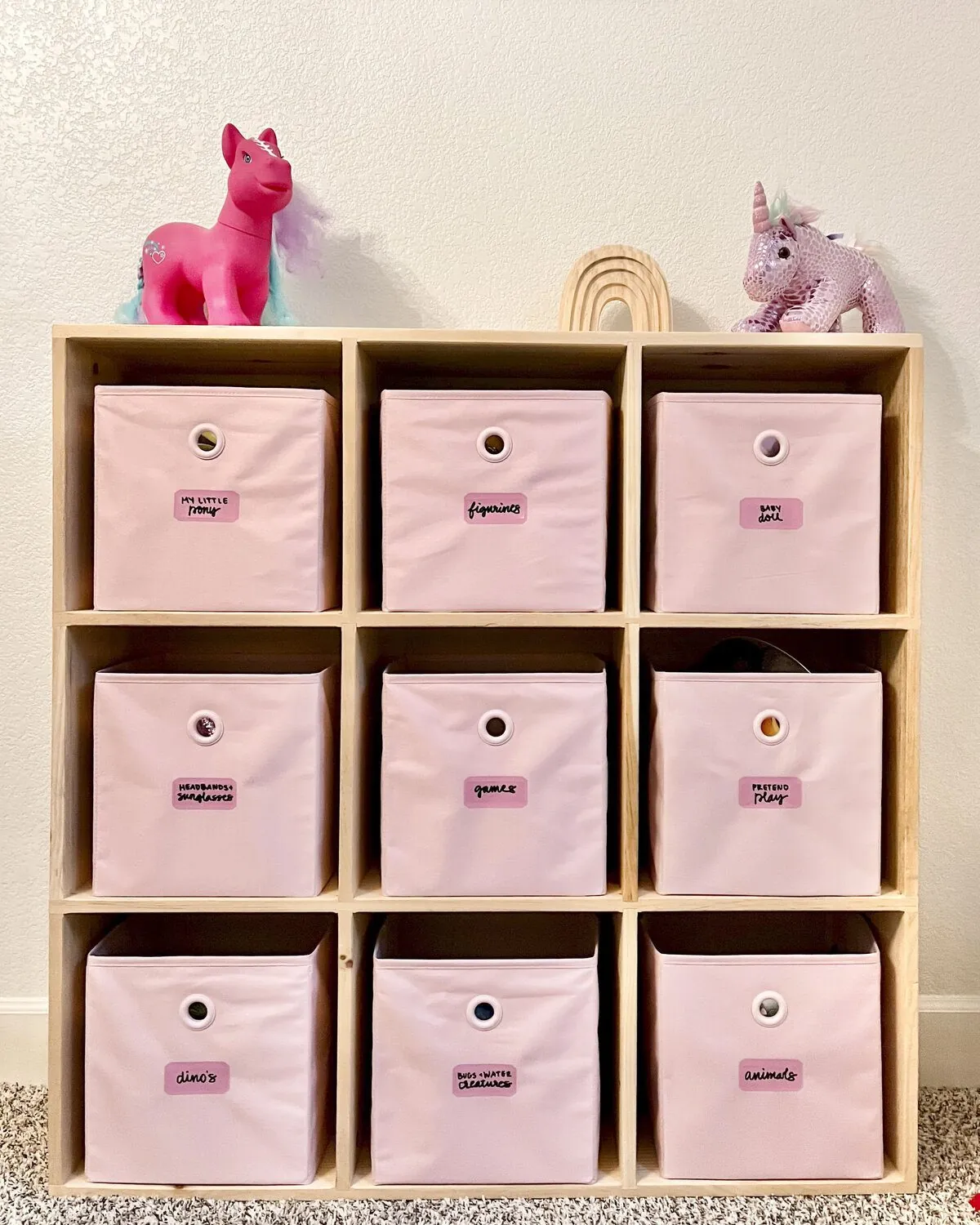 A wooden cube organizer with pink fabric bins, each with a label
