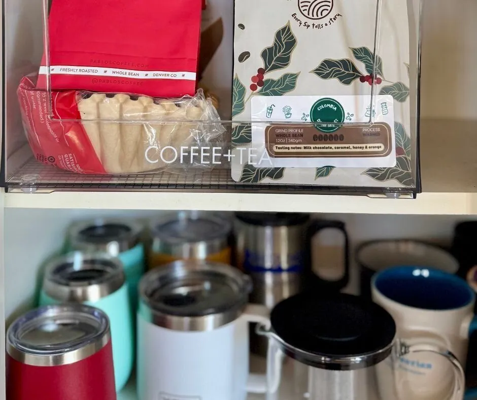 A clear bin labeled Coffee + Tea above a row of travel mugs