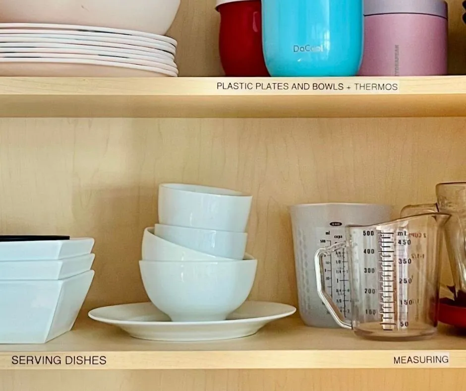Kitchen cabinet shelves labeled Serving Dishes, Measuring and Plastic Plates and Bowls
