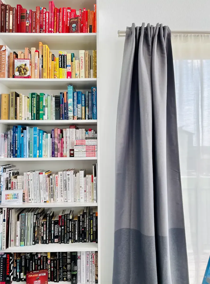 Bookshelf organized by color beside a window
